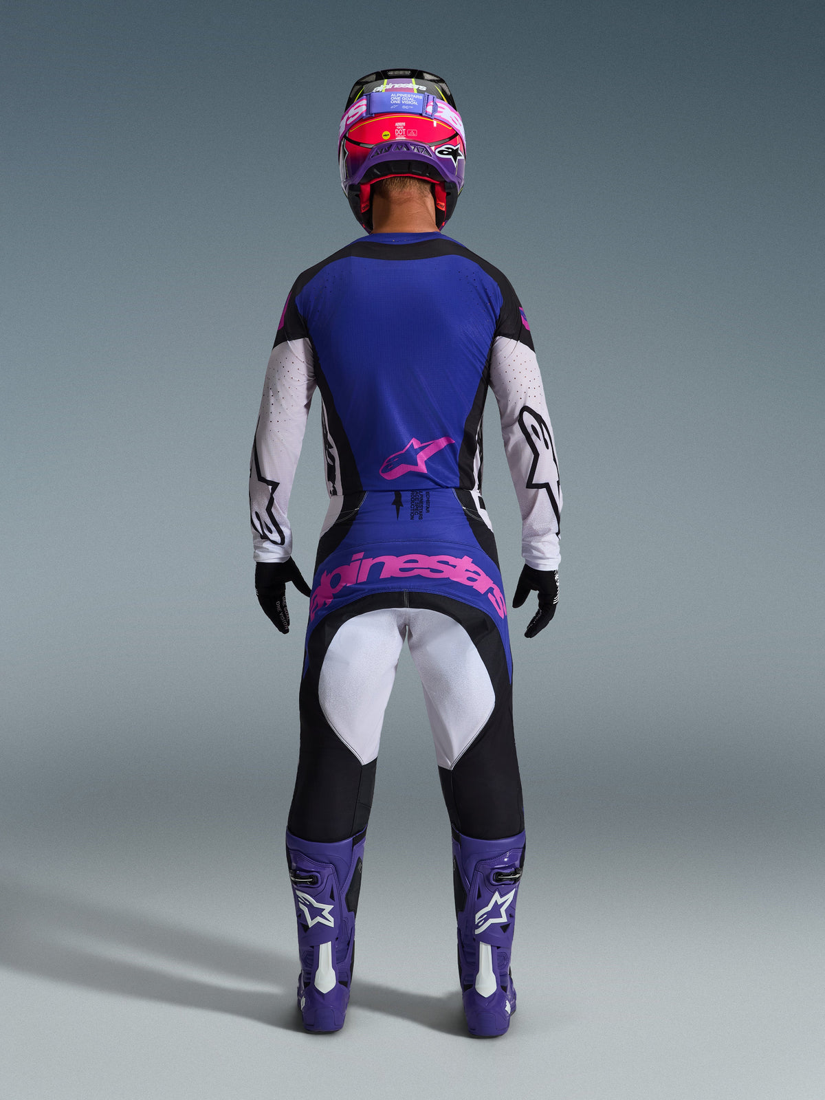 Alpinestars 2026 Techstar Knif Gear Set, vista trasera de piloto de motocross, negro, gris claro y morado con logotipo rosa, combinado con botas y casco morados a juego, equipamiento de competición profesional para rendimiento off-road