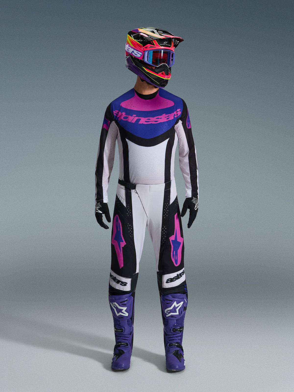 Alpinestars 2026 Techstar Knif Gear Set, equipo completo de motocross, blanco, negro, morado y rosa, usado con casco multicolor, gafas azules, botas moradas y guantes negros, kit coordinado de alto rendimiento para carreras off-road