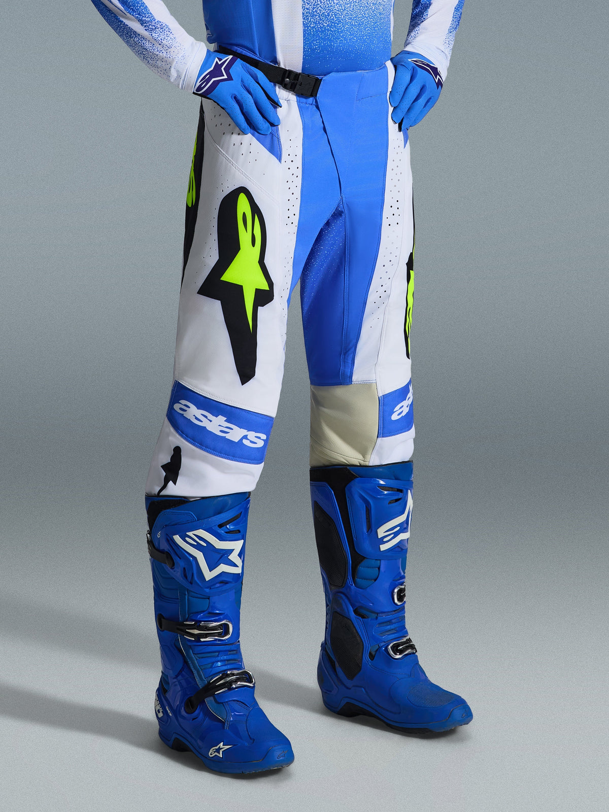 Alpinestars Techstar Knif Pants 2026, pantalones de motocross, azul UCLA, negro y amarillo flúor, usados con botas y guantes de motocross azules a juego, con paneles blancos, grandes logotipos de estrellas en amarillo flúor y diseño atlético todoterreno