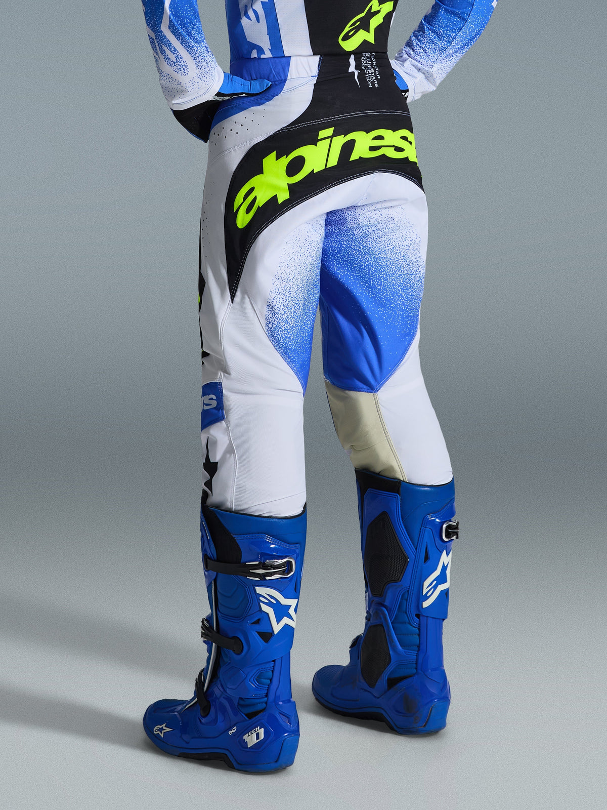 Alpinestars 2026 Techstar Knif Pants, pantalones de motocross, azul UCLA, negro y amarillo flúor, vista trasera con un llamativo logotipo de Alpinestars en amarillo neón, chasis blanco con gráficos en degradado azul, combinados con botas de motocross de alto rendimiento en azul brillante.