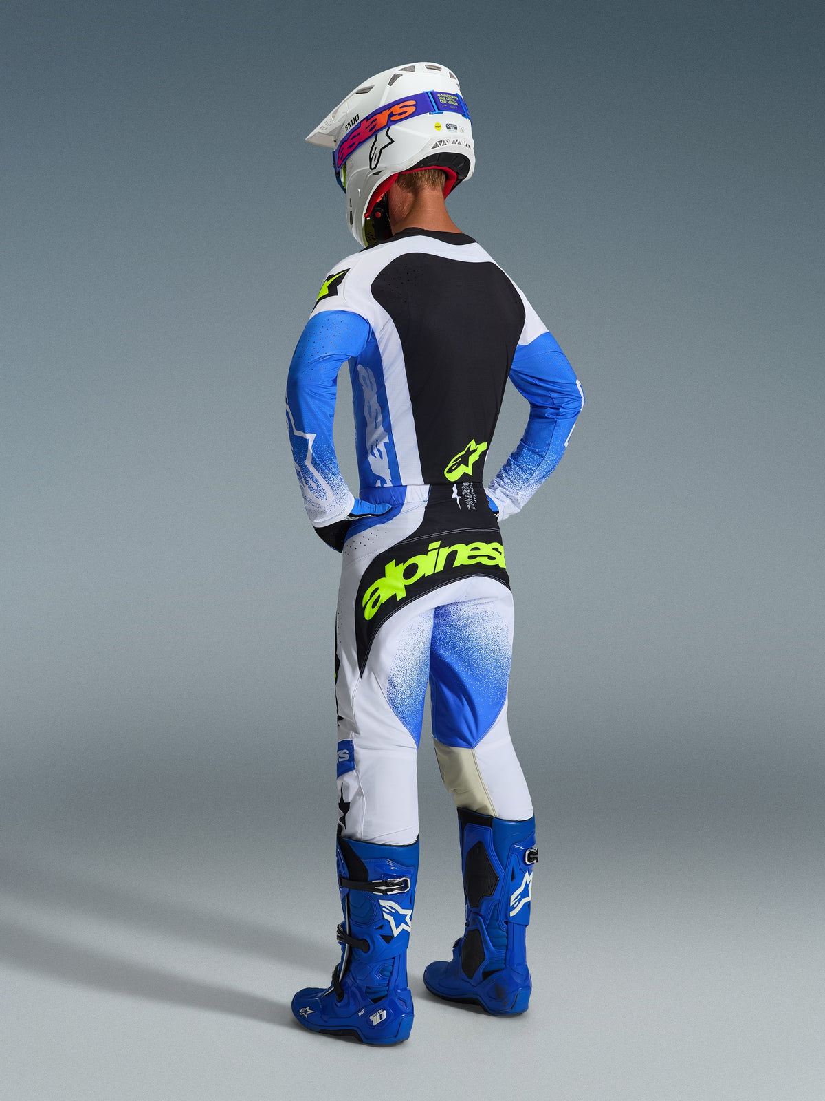 Piloto de motocross visto desde atrás con los pantalones 2026 Techstar Knif en azul Ucla, negro y amarillo flúor, destacando el logotipo amarillo brillante en el asiento, jersey coordinado con mangas azules, casco blanco y botas de motocross azules.