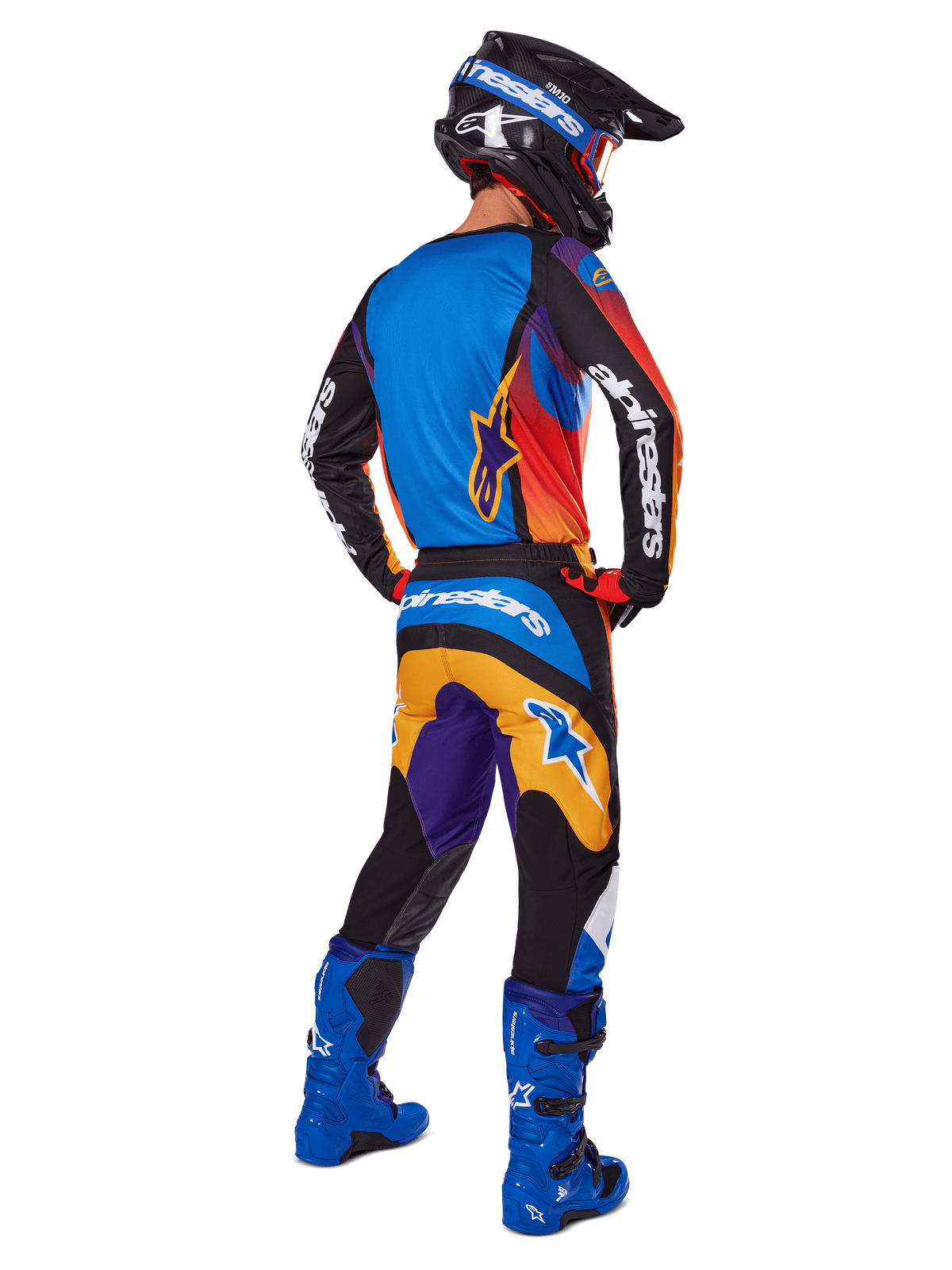 Piloto de motocross visto desde atrás con pantalones Alpinestars Fluid Wurx 2025, diseño multicolor con detalles en azul, naranja, amarillo y púrpura, combinados con un jersey a juego, botas azul brillante y casco negro, equipamiento completo de competición off-road