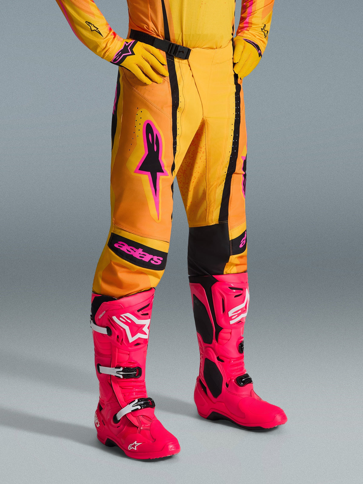 Alpinestars 2026 Techstar Nomur Pants, pantalones de motocross, naranja, amarillo y rosa, combinados con jersey y guantes amarillos a juego y botas rosa brillante, ajuste atlético de competición con logotipos rosas y hebilla magnética negra, equipamiento vibrante para competición off-road