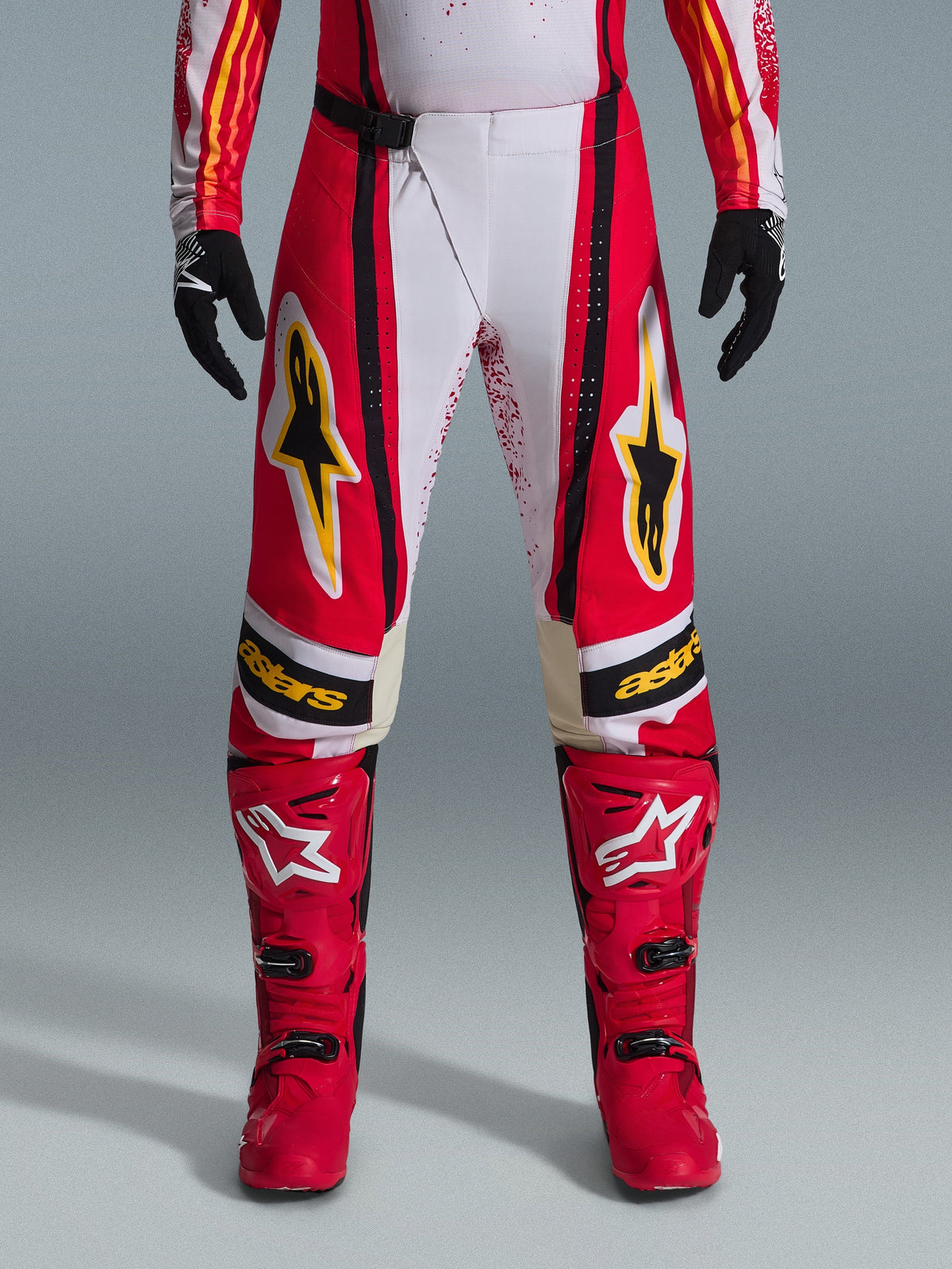 Alpinestars Techstar Nomur Pants 2026, pantalones de motocross, rojos y blancos con detalles en negro y amarillo, usados con botas rojas a juego y guantes negros, equipamiento de carreras off-road de alto rendimiento