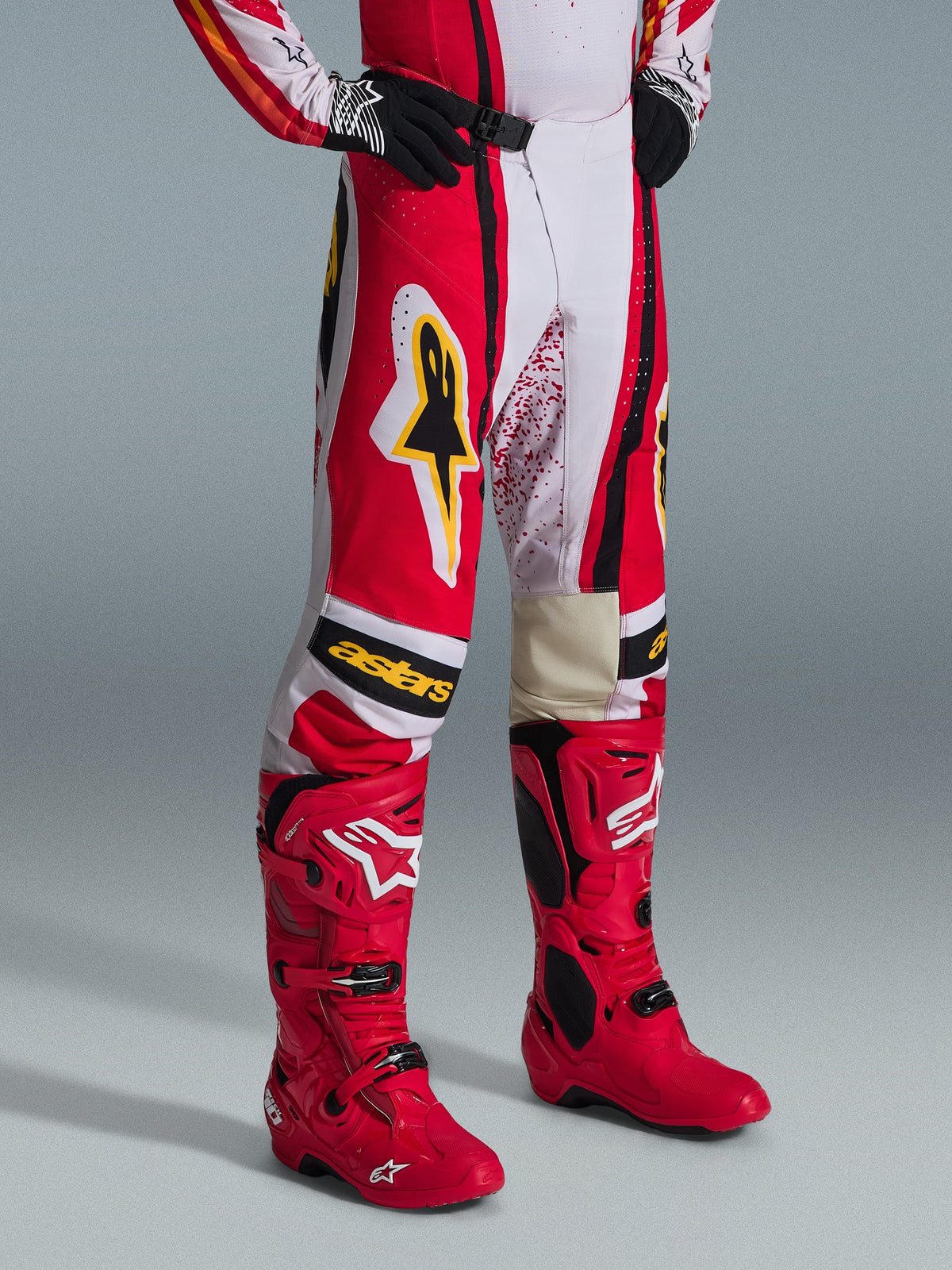 Alpinestars 2026 Techstar Nomur Pants, pantalones de motocross rojos, blancos y negros con detalles amarillos, combinados con botas rojas y guantes negros, con logo amarillo de Alpinestars y marca "astars" en las rodillas, equipamiento profesional para carreras off-road