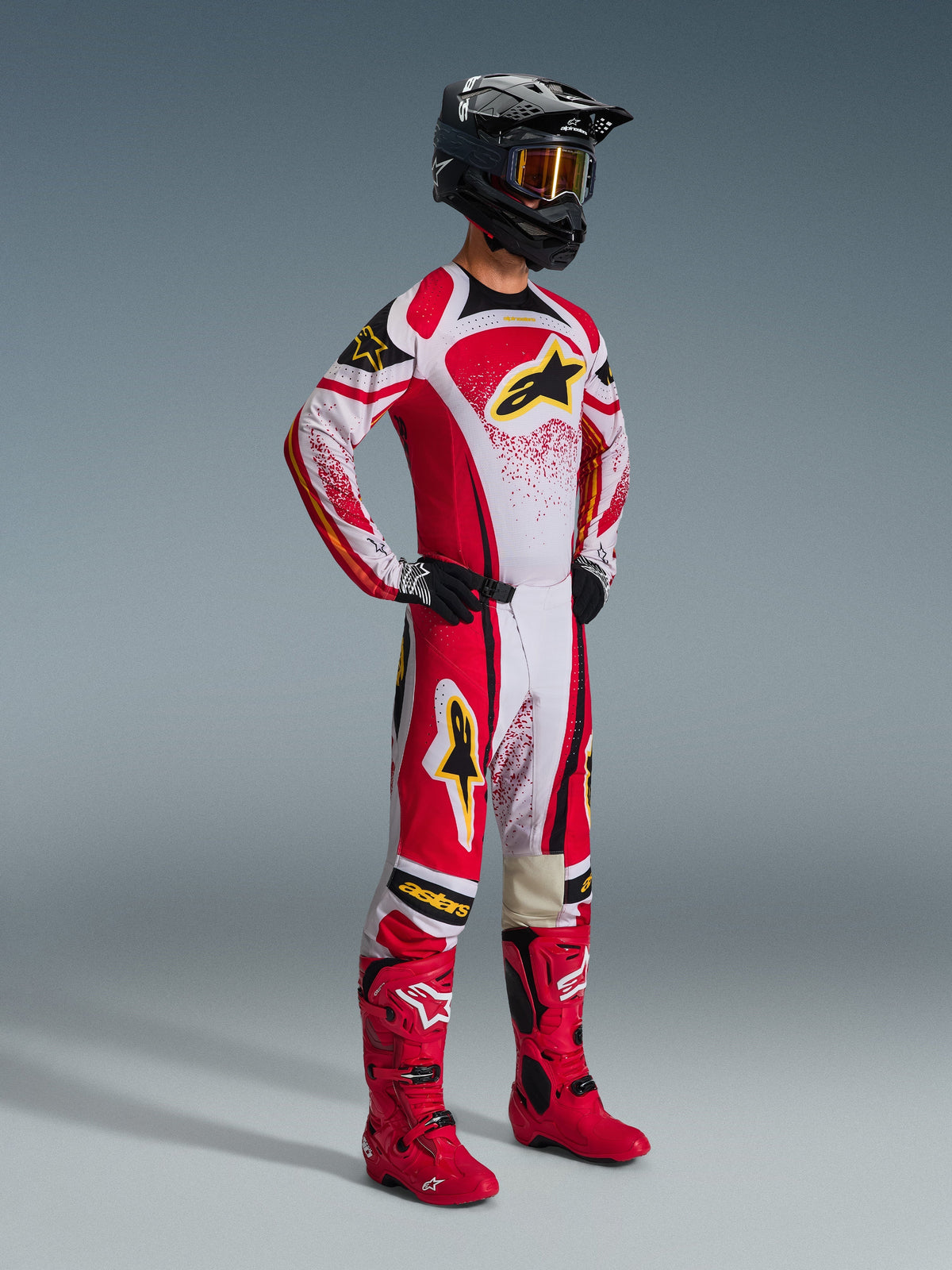 Alpinestars 2026 Techstar Nomur Pants, pantalones de motocross, rojos y blancos con detalles en negro y amarillo, usados por un piloto con jersey de carreras a juego, botas rojas brillantes y casco negro con gafas doradas, equipo profesional completo de competición