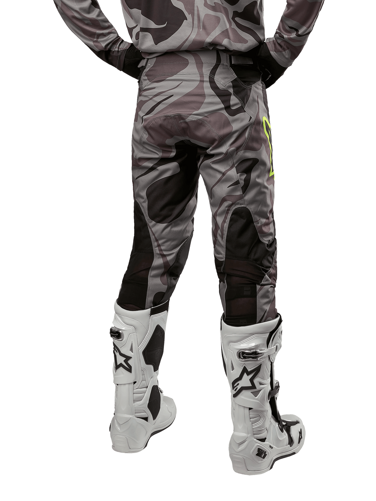 Alpinestars 2024 Racer Tactical Pants, pantalones de motocross, color Cast Gray Camo Magnet, vista trasera que muestra el patrón de camuflaje y paneles elásticos negros transpirables, usados con botas de motocross blancas y negras, diseñados para competición off-road.