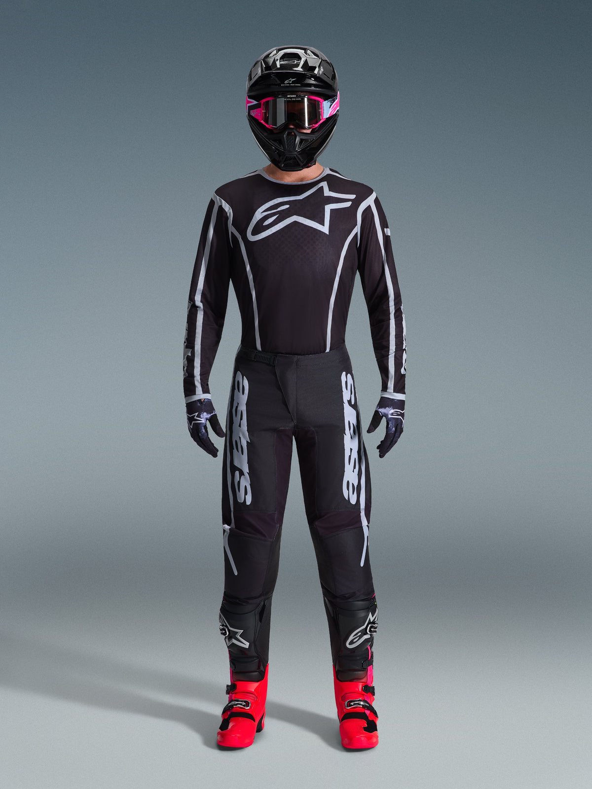 Alpinestars 2026 Fluid Apex Gear Set, Motocross Outfit, Black with Gray accents, jersey featuring large white Astars logo, matching pants with bold branding, black helmet with pink goggles, and bright red boots, complete off-road racing kit