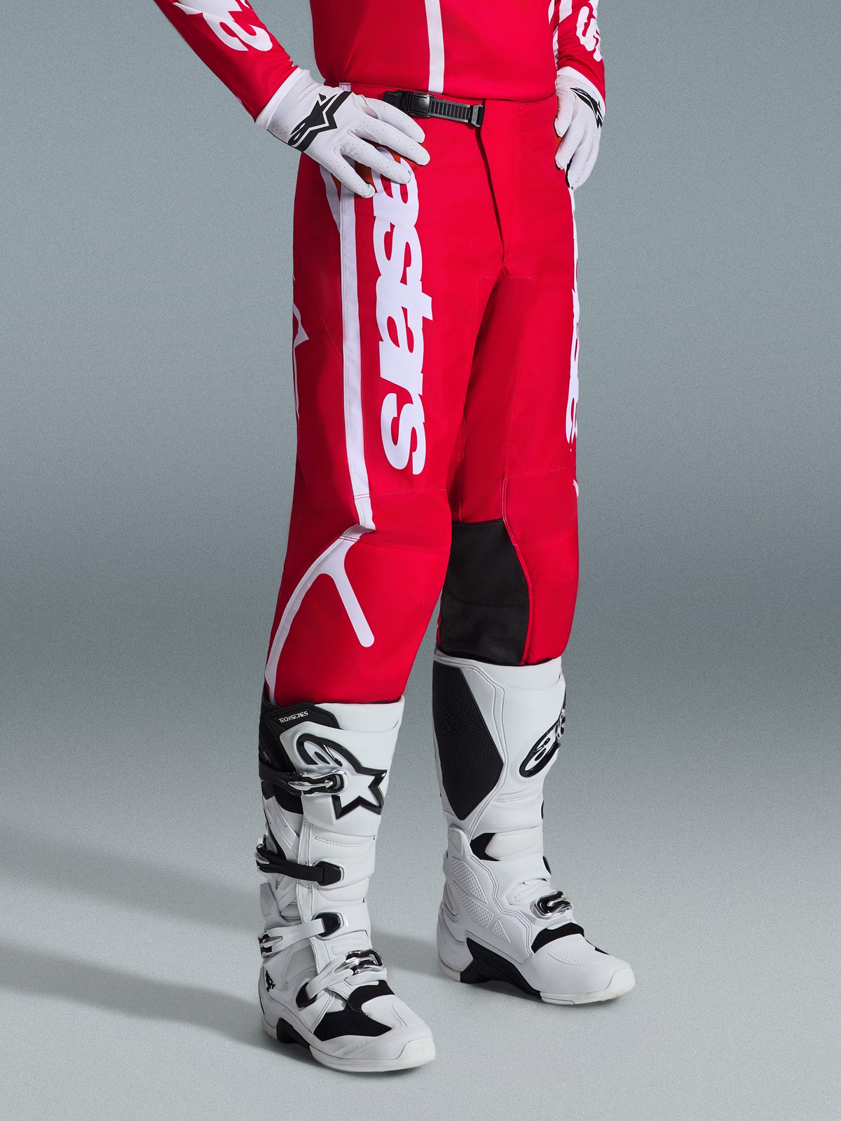 Pantalones Alpinestars Fluid Apex 2026, pantalones de motocross, rojos y blancos, usados con botas y guantes de motocross blancos y negros, con logotipos blancos llamativos y paneles negros en el interior de las rodillas, diseñados para el rendimiento off-road