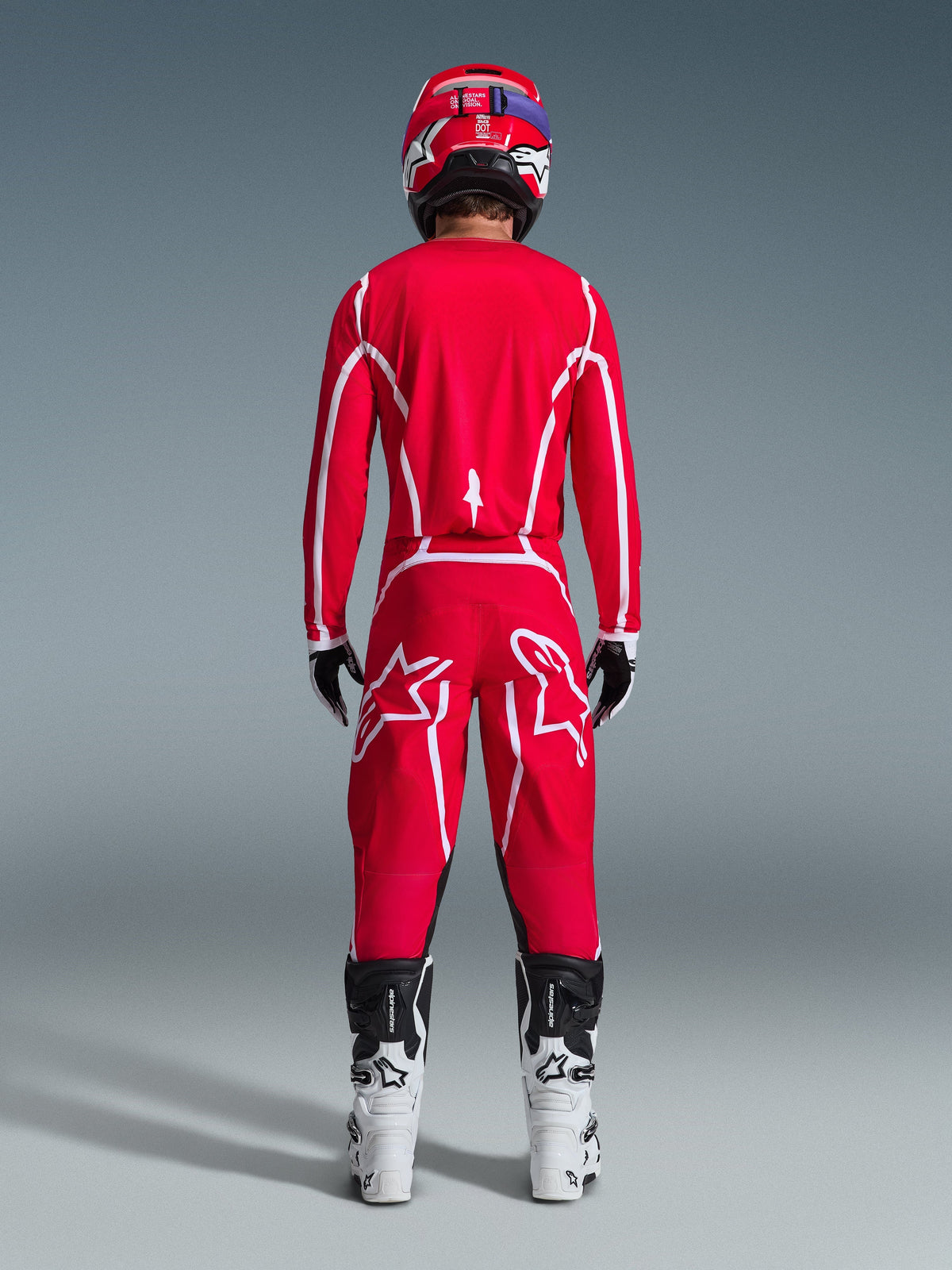 Alpinestars 2026 Fluid Apex Pants, pantalones de motocross, rojos y blancos, vista trasera con jersey a juego, casco rojo y botas blancas y negras, con grandes logotipos Astar blancos en las piernas, conjunto coordinado para carreras todoterreno