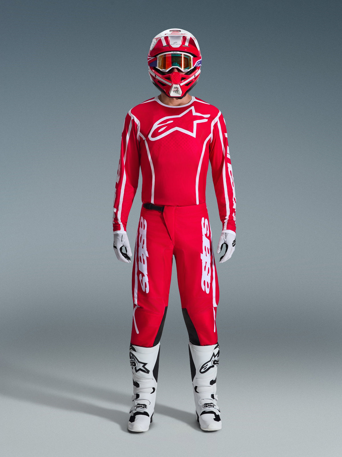Pantalones Alpinestars Fluid Apex 2026, pantalones de motocross, rojos y blancos, usados como un conjunto completo de equipamiento de competición con jersey rojo a juego, botas blancas y casco rojo y blanco, con marca destacada y paneles negros para rendimiento off-road.
