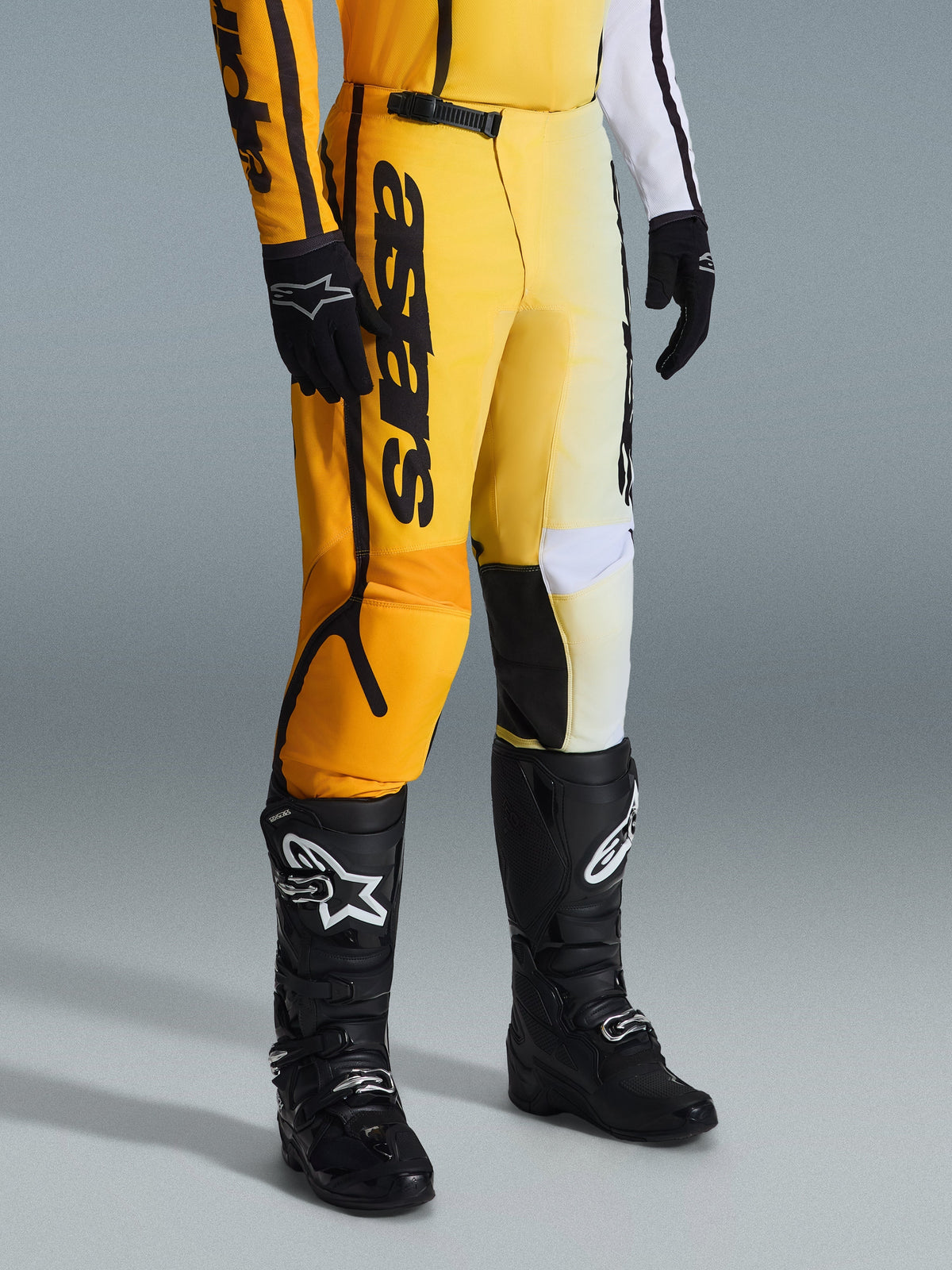 Alpinestars 2026 Fluid Apex Pants, pantalones de motocross, amarillos y negros, usados con botas y guantes negros, con el logotipo 'astars' destacado en el muslo, diseño ergonómico con paneles reforzados, material duradero para conducción todoterreno