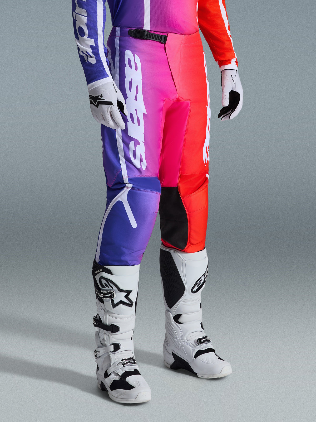 Pantalones Alpinestars 2026 Fluid Apex, pantalones de motocross, degradado multicolor púrpura, rosa y rojo, combinados con botas y guantes de motocross en blanco y negro, con marca vertical blanca y detalles negros en las rodillas, equipamiento de alto rendimiento para off-road