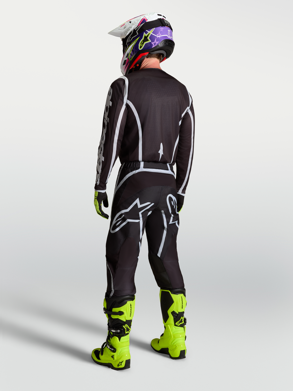 Alpinestars Men's Fluid Apex V2 Motocross Pants in Black and Silver, shown from behind with matching jersey and neon boots.