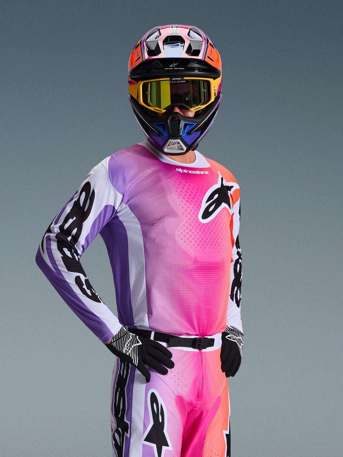 Piloto de motocross con el Jersey Alpinestars 2026 Racer Air Portl, diseño con degradado multicolor en rosa, púrpura y naranja con detalles blancos, casco colorido a juego y gafas amarillas, guantes negros, equipamiento profesional de carreras off-road