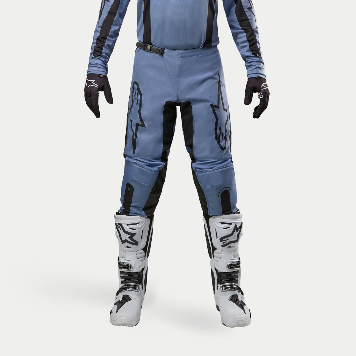 Pantalones Alpinestars Fluid Lurv 2024, pantalones de motocross, azul claro y negro, usados con botas de carreras blancas y negras y guantes a juego, con logotipos de estrellas negras en los muslos y diseño ergonómico para rendimiento todoterreno