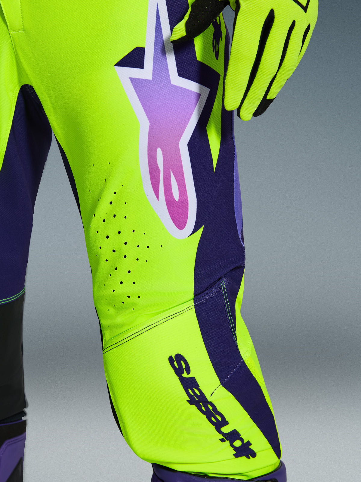 Pantalones Alpinestars 2026 Supertech Vista, pantalones de motocross, amarillo, púrpura y negro, vista de cerca de la pierna con paneles amarillo neón y púrpura oscuro, logotipo de estrella grande en degradado púrpura, perforaciones de ventilación cortadas con láser, equipamiento de competición profesional