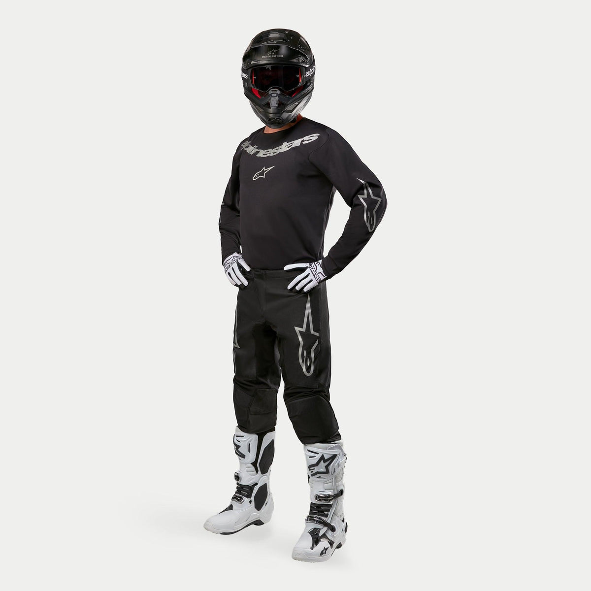 Alpinestars 2024 Fluid Graphite Pants, pantalones de motocross, negro y plata, usados con jersey negro a juego, casco negro, guantes blancos y botas blancas, con logotipos Alpinestars plateados en los muslos, ajuste atlético ergonómico para carreras fuera de carretera