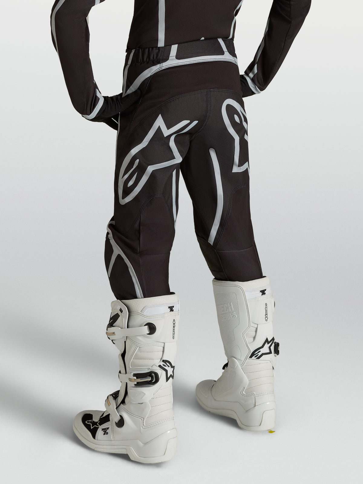 Alpinestars Fluid Apex V2 juvenil, pantalones de motocross negros y plateados, vista trasera con botas blancas, protección