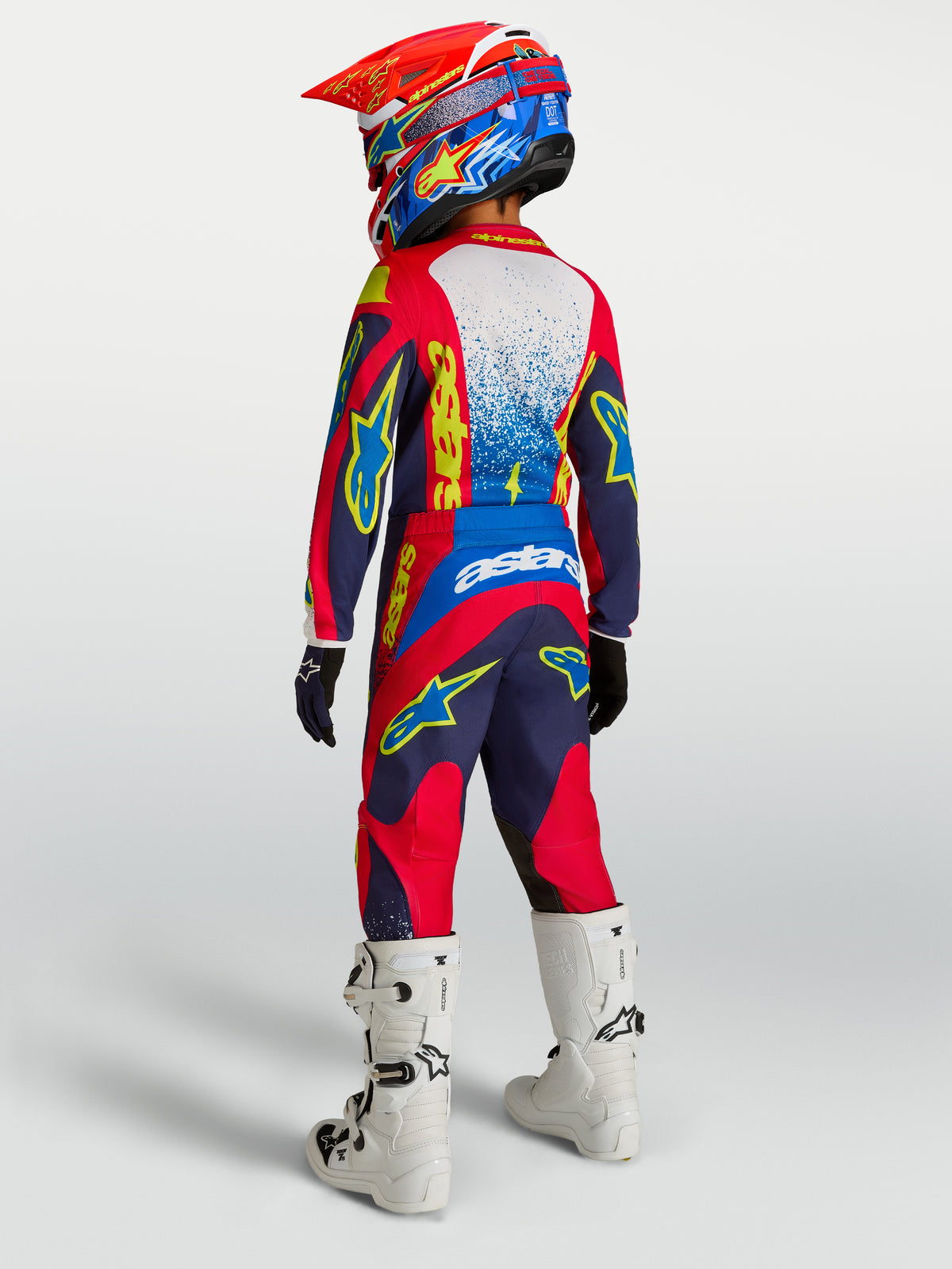 Alpinestars Fluid Drag juvenil, pantalones de motocross azul marino y rojo fuego con asiento reforzado y botas blancas.
