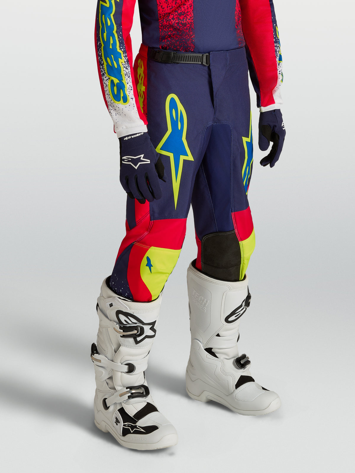 Pantalones Alpinestars Fluid Drag Juvenil de motocross, azul marino y rojo con detalles neón y botas blancas.