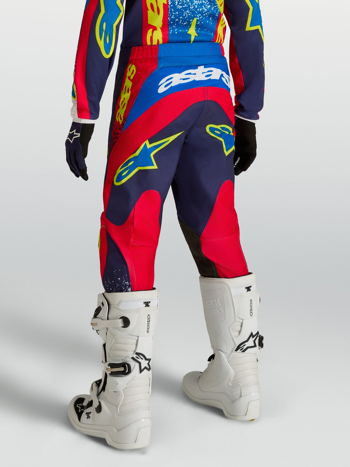 Alpinestars Pantalones Fluid Drag Juvenil, pantalones de motocross azul marino y rojo, vista trasera con botas blancas.