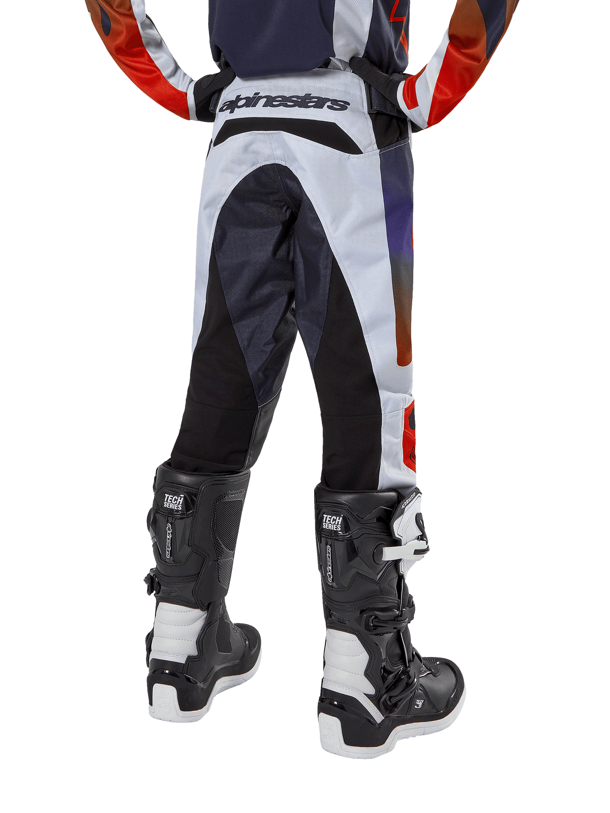Alpinestars 2024 Youth Racer Hoen Pants, pantalones de motocross juveniles, gris claro con detalles en naranja intenso y negro, vista trasera con paneles negros en el asiento y las piernas, marca destacada en la parte trasera de la cintura, combinados con botas de motocross blancas y negras para carreras todoterreno