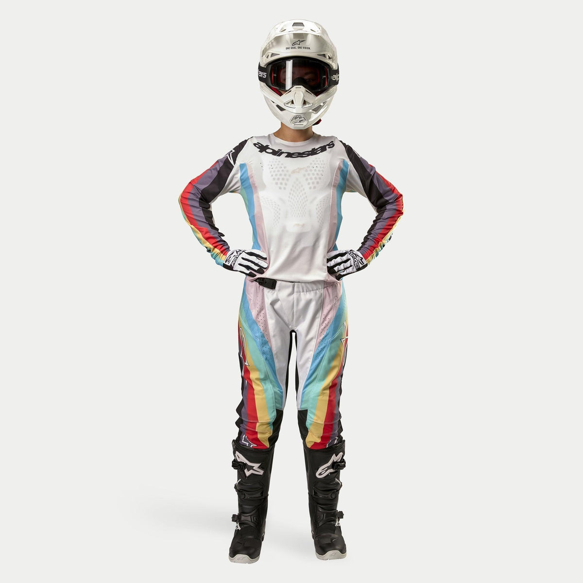 Piloto de motocross con pantalones Alpinestars Stella Techstar para mujer 2024, Negro Multicolor con base blanca y franjas rojas, amarillas y azules, jersey de manga larga a juego, casco blanco y botas negras, equipo completo de carreras para competición todoterreno