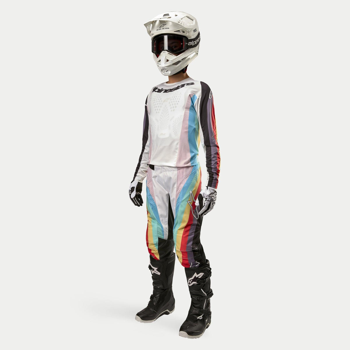 Piloto de motocross con pantalones Alpinestars Stella Techstar 2024 para mujer, pantalones de motocross, negro multicolor con paneles blancos y franjas diagonales vibrantes, jersey a juego, casco blanco y botas negras, conjunto de carreras todoterreno coordinado para mujer