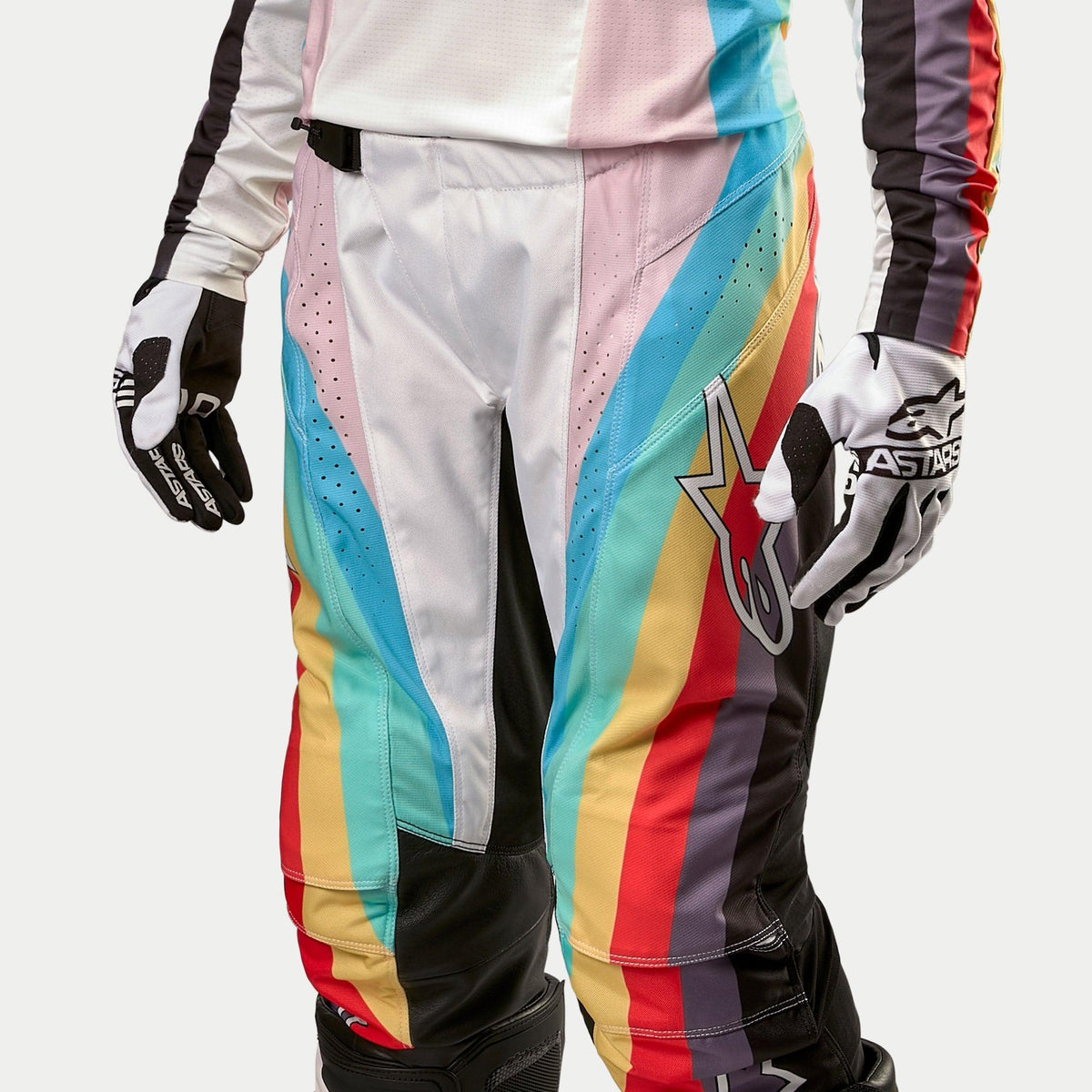 Pantalones Alpinestars Stella Techstar 2024 para mujer, pantalones de motocross, negro multicolor con vibrantes franjas diagonales en azul, rosa, amarillo y rojo, con un gran logotipo de estrella en el muslo, mostrados con jersey y guantes a juego, equipamiento profesional de competición todoterreno