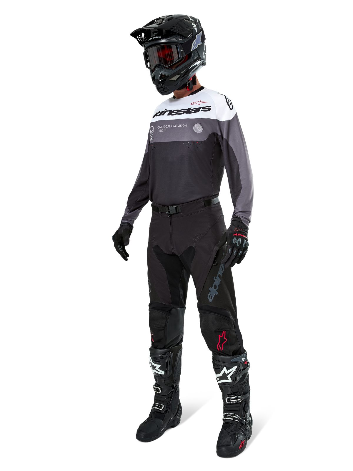 Alpinestars Pro-Dura Jersey in Black Magnet White, worn by a motocross rider in full gear including black pants, black helmet with goggles, and black and white boots. The jersey features a technical color-blocked design with white, grey, and black panels, engineered for enduro and off-road performance.
