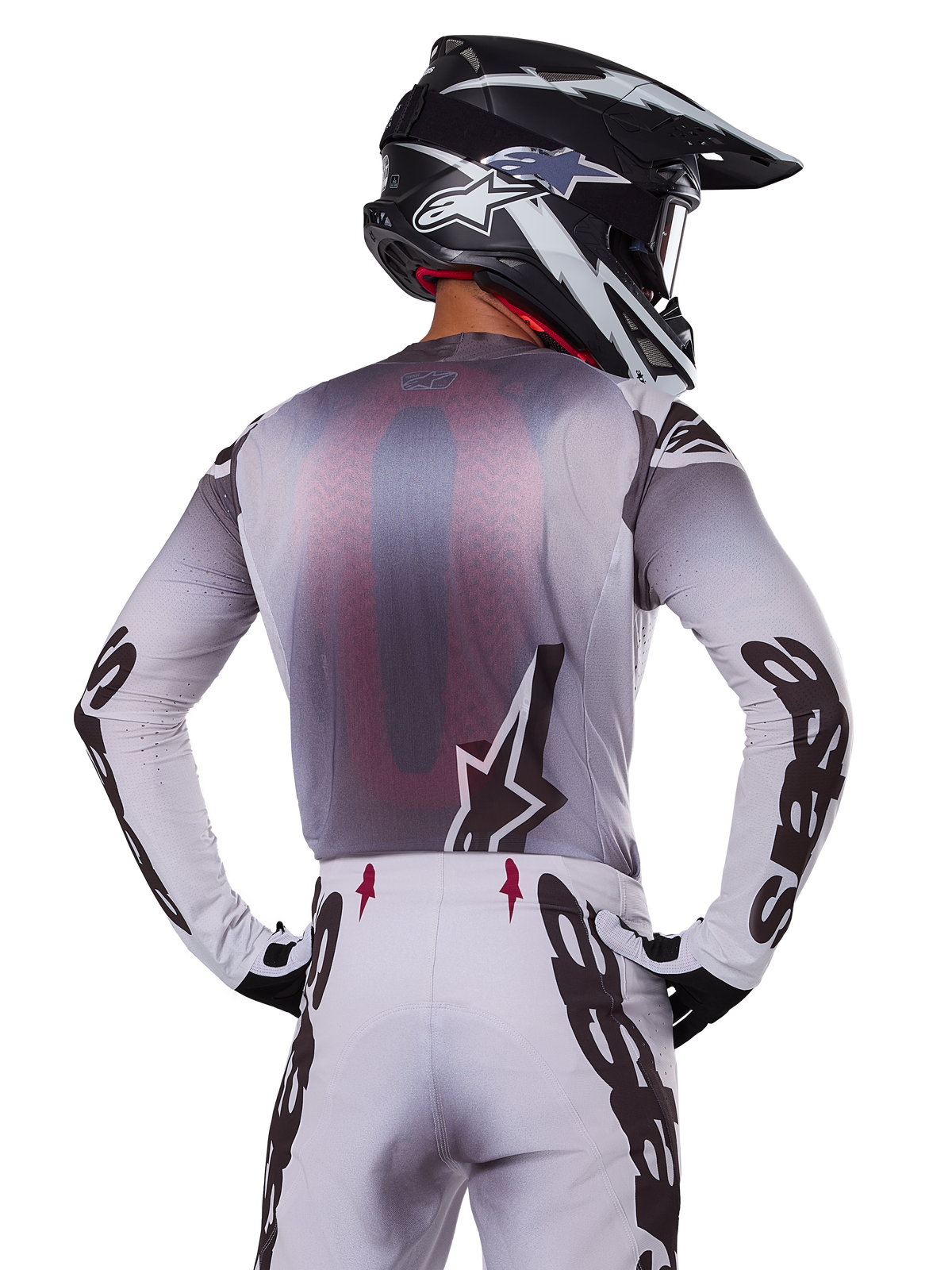 Conjunto de equipo Alpinestars Supertech Maker 2025, piloto de motocross visto desde atrás, jersey blanco y gris con logotipos negros grandes en las mangas y logo de estrella, pantalones blancos a juego con gráficos negros, casco blanco y negro, traje de carreras todoterreno profesional