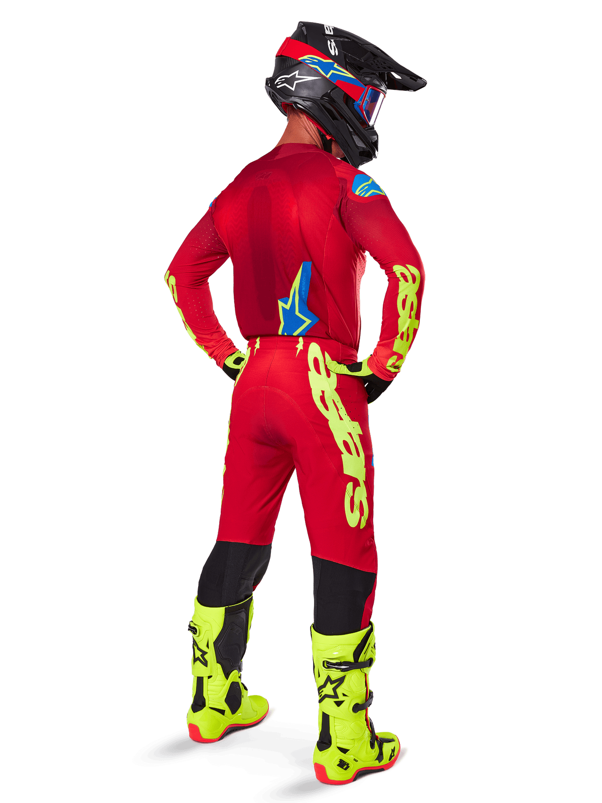 Piloto de motocross en vista trasera con el conjunto Alpinestars 2025 Supertech Maker, jersey rojo brillante con logotipos en amarillo flúor, pantalones rojos a juego con detalles amarillos, casco negro con elementos rojos y azules, botas en amarillo flúor, equipamiento profesional coordinado para rendimiento todoterreno.