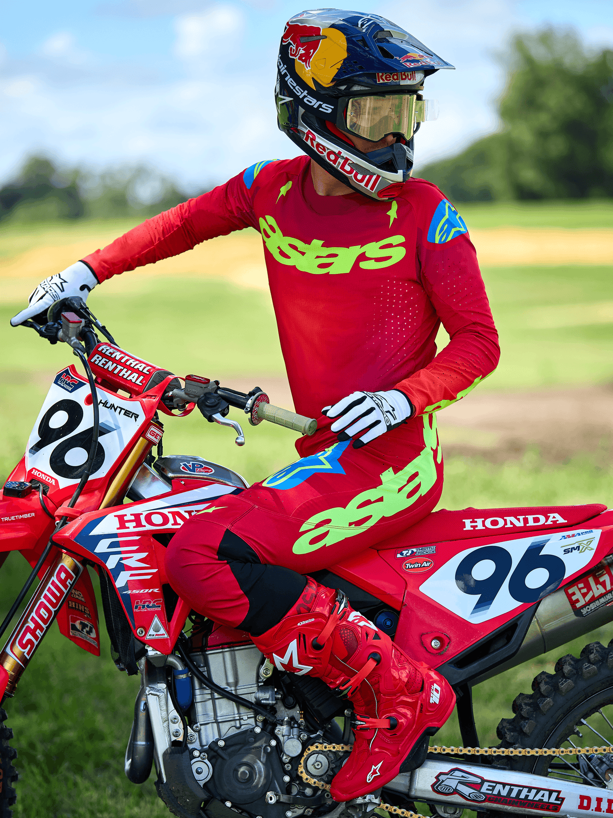 Piloto de motocross vistiendo el jersey Alpinestars 2025 Supertech Maker en rojo brillante con el logotipo 'astars' en amarillo neón, combinado con pantalones y botas rojas a juego, guantes blancos y negros, sentado sobre una moto de carreras Honda roja en un entorno al aire libre