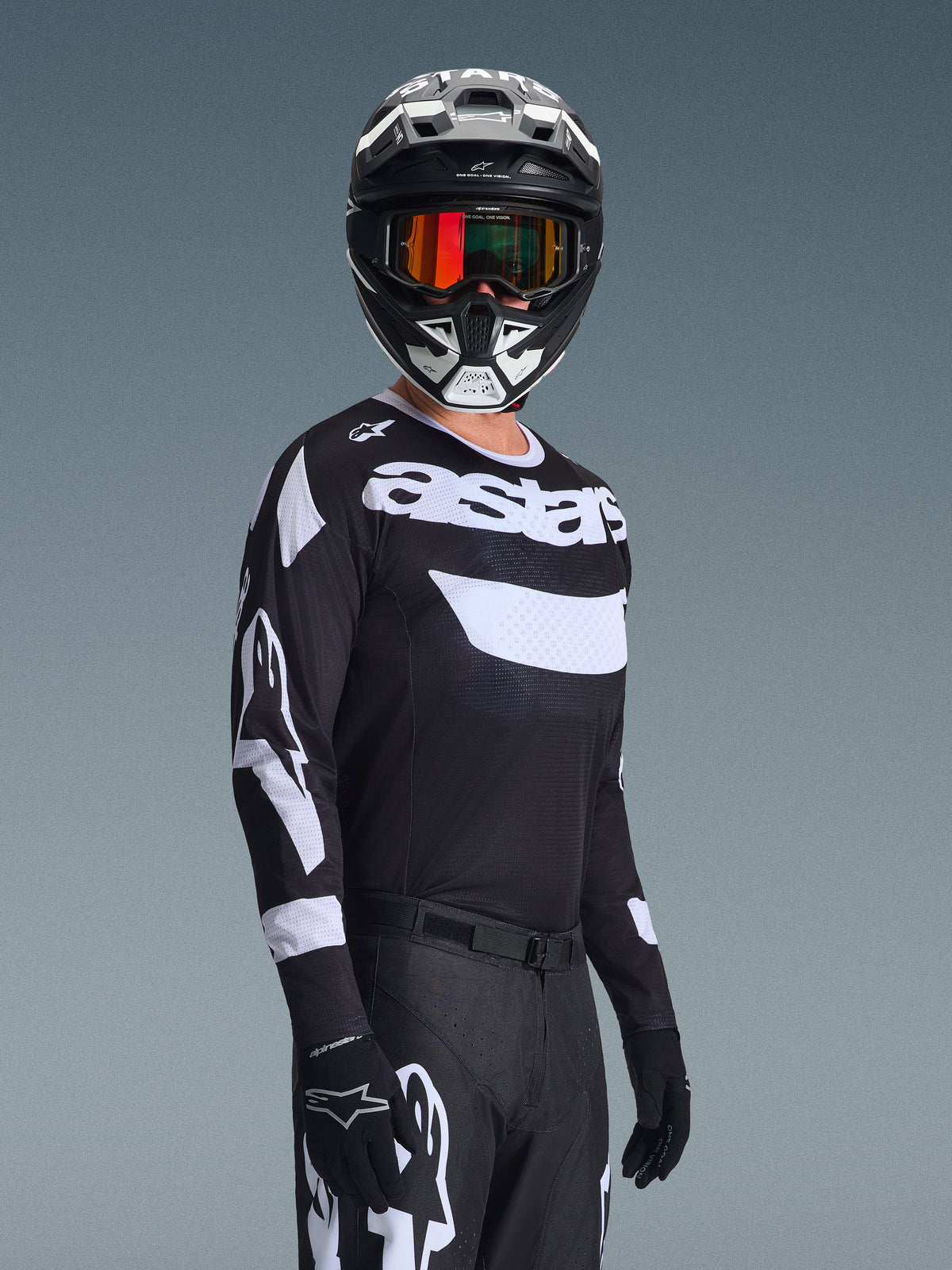 Motocross rider wearing the 2026 Racer Air Riway Jersey, Black and White jersey with 'astars' logo, matching black and white helmet with orange mirrored goggles, black motocross pants and gloves, coordinated outfit for off-road racing
