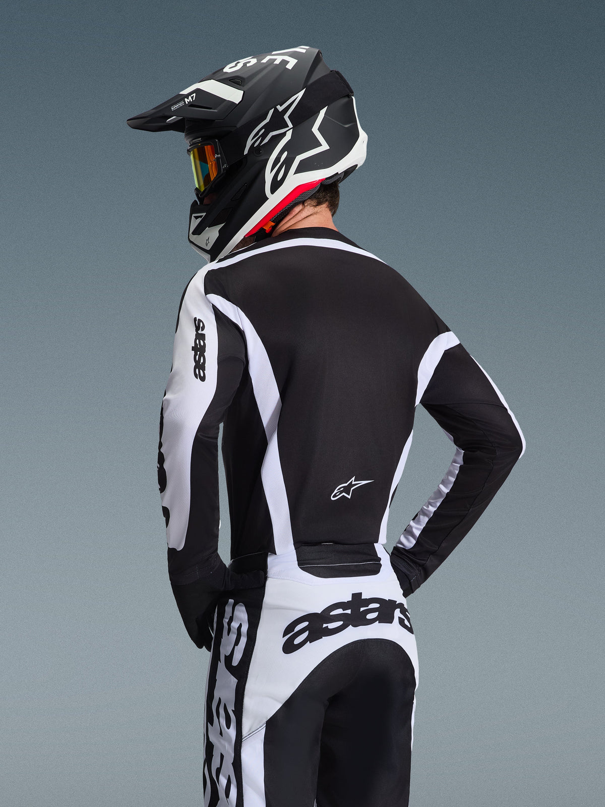 Alpinestars 2026 Racer Riway Gear Set, piloto de motocross visto desde atrás con jersey técnico y pantalones en blanco y negro, casco a juego con gafas, logotipos llamativos de astars en las mangas y en la parte posterior, diseñado para el rendimiento off-road