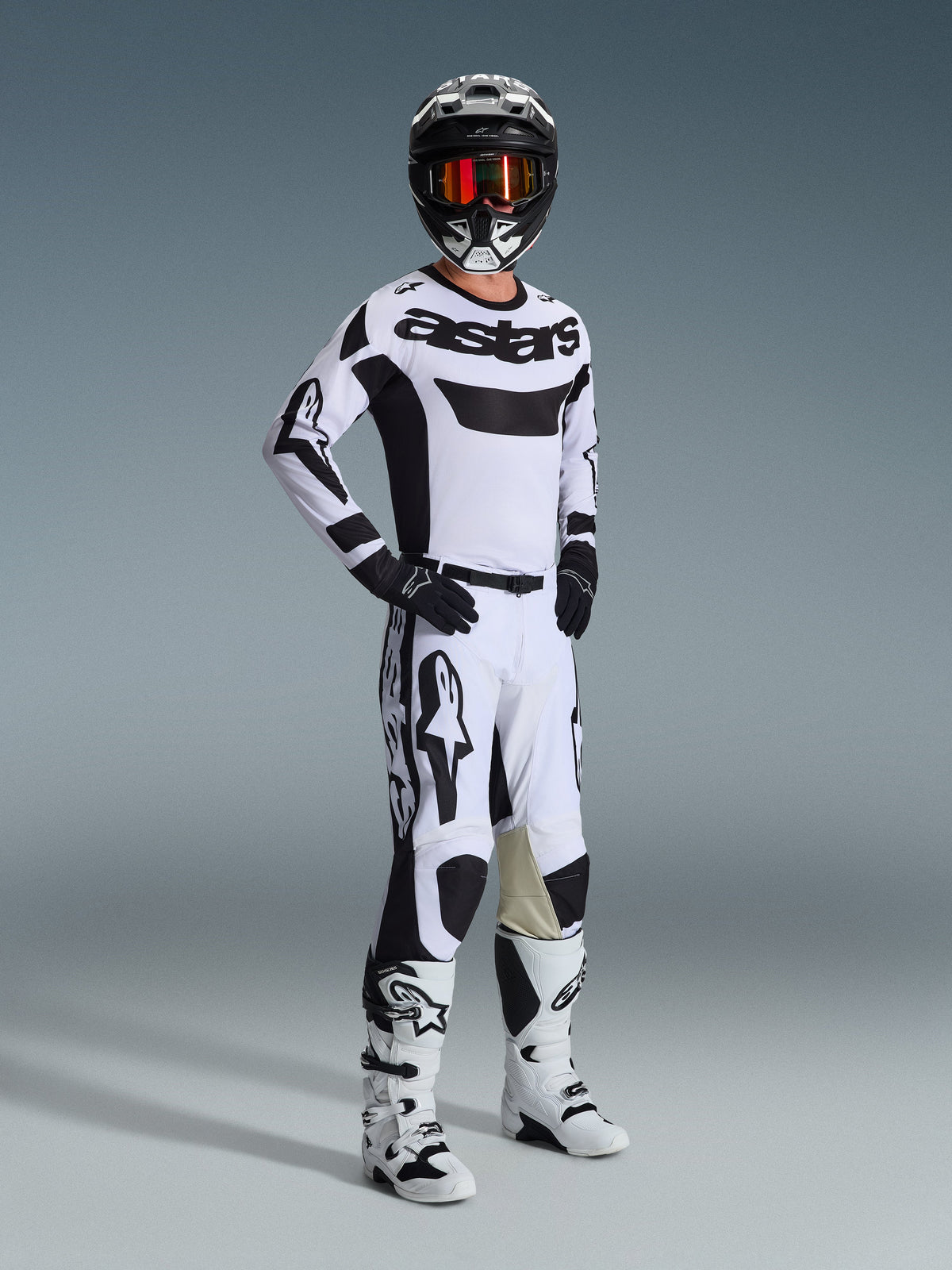 Alpinestars 2026 Racer Riway Gear Set, piloto de motocross con kit de carreras blanco y negro, jersey blanco con logo 'astars' negro en el pecho, pantalones blancos con detalles negros, casco negro con gafas naranjas, botas blancas, equipamiento coordinado para motocross y conducción off-road