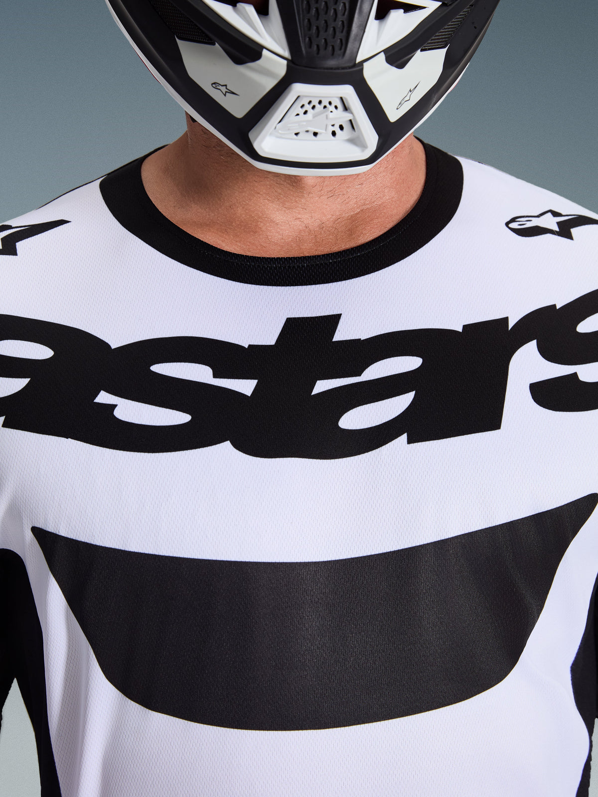 Primer plano de un piloto con el Jersey Alpinestars Racer Riway 2026 en blanco y negro, con el llamativo logotipo 'astars' en el pecho y cuello redondo negro, combinado con un casco de motocross a juego.