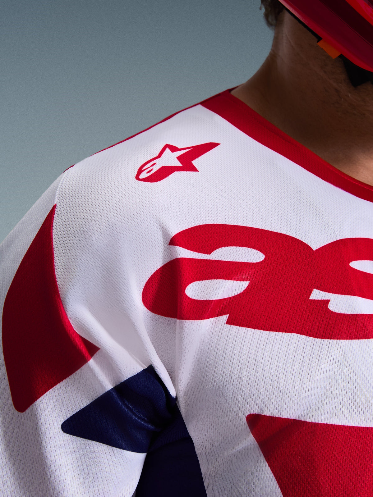 Primer plano del Alpinestars 2026 Racer Riway Jersey, jersey de motocross en blanco, azul y rojo, con textura de malla transpirable que absorbe la humedad, logo de estrella roja en el hombro y gráficos rojos llamativos en el pecho