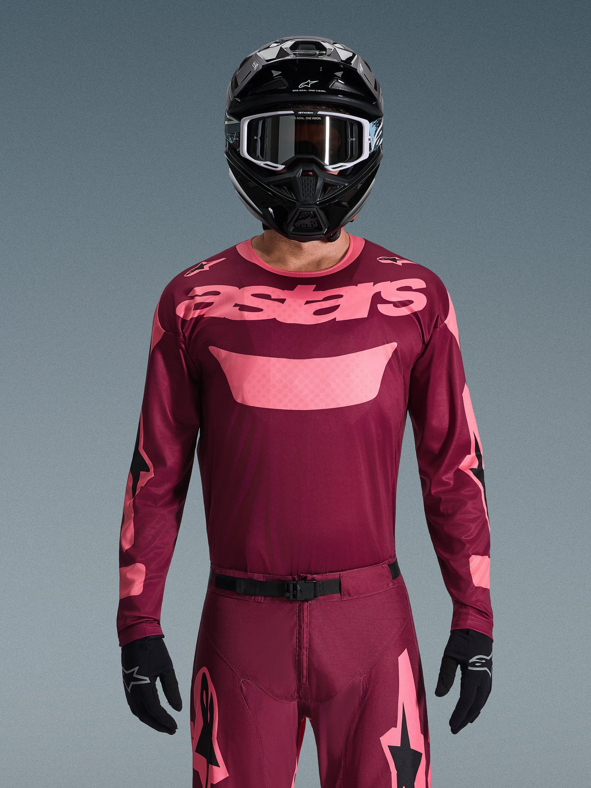 Piloto de motocross con el conjunto de equipo Alpinestars 2026 Racer Riway en granate y rosa, jersey con logotipo rosa destacado en el pecho, pantalones a juego con detalles negros y rosas, casco integral negro con gafas y guantes negros, equipamiento de carreras off-road coordinado