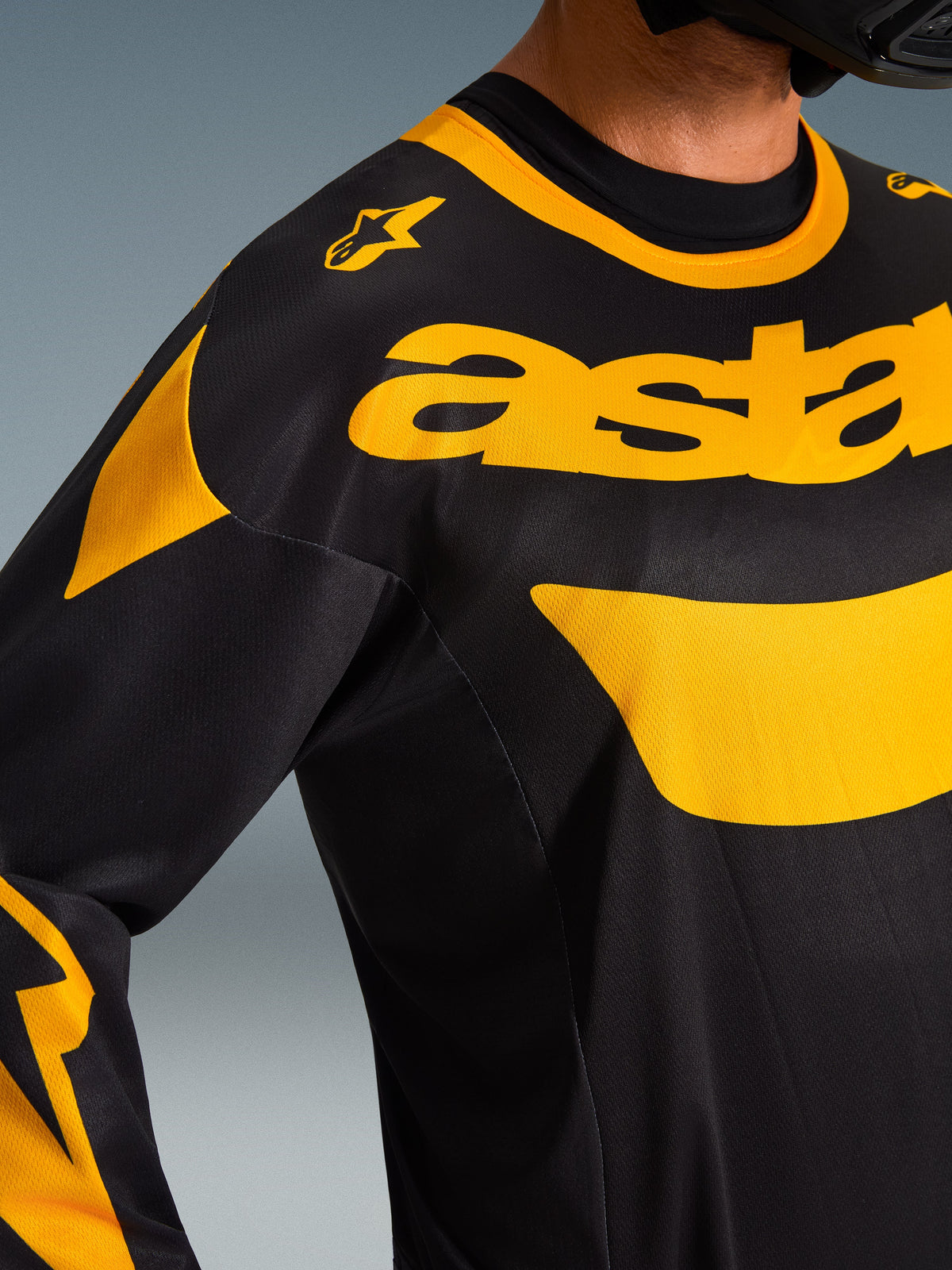 Primer plano del jersey Alpinestars Racer Riway 2026, negro y amarillo, con logotipos amarillos llamativos en el pecho, construcción en tejido de malla técnica para ventilación, ropa de motocross de alto rendimiento