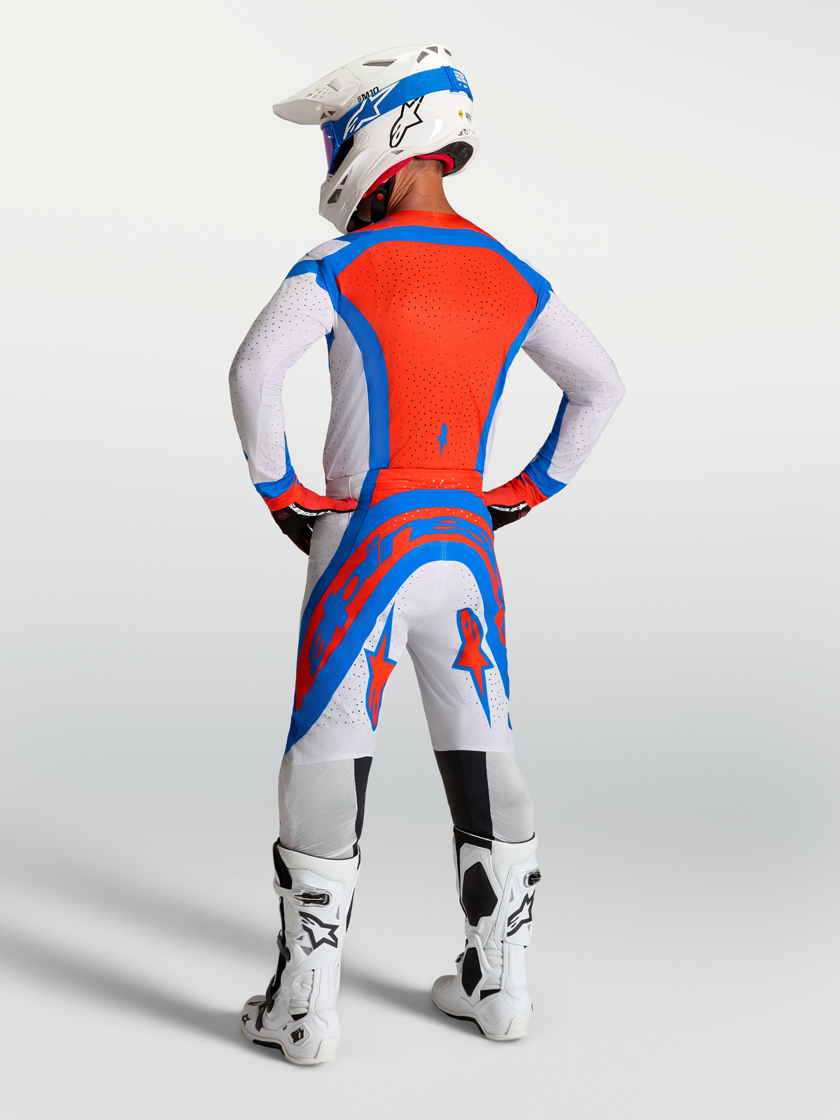 Conjunto Alpinestars Supertech Vesta de motocross, lila claro y rojo cardenal, vista trasera en piloto con casco y botas.