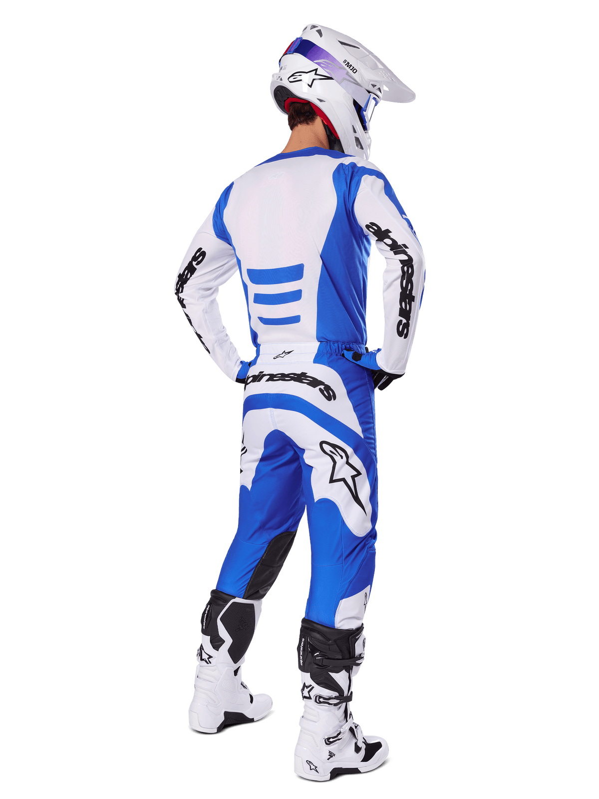 Piloto de motocross desde atrás vistiendo el conjunto Alpinestars Fluid Haul 2025, jersey azul y blanco con pantalones a juego, casco blanco con acentos azules y botas de carreras blancas y negras, atuendo coordinado de carreras todoterreno