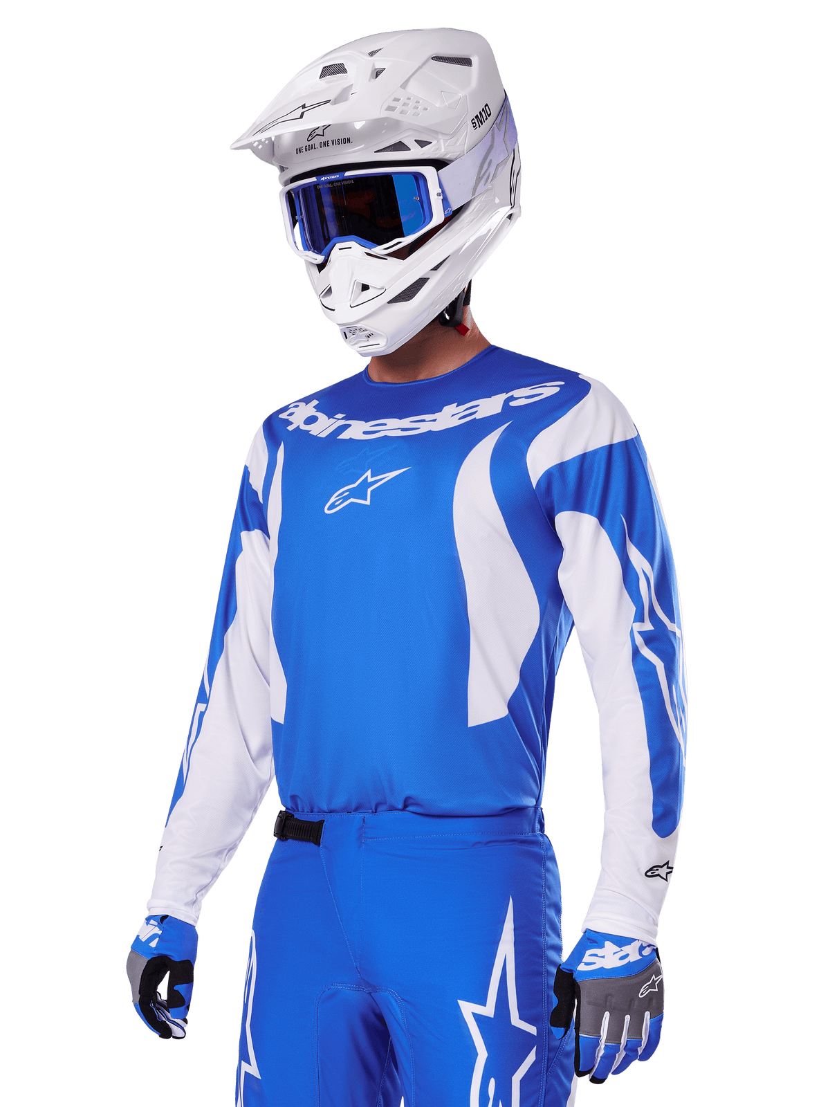 Piloto de motocross con el conjunto de equipo Alpinestars 2025 Fluid Haul en azul y blanco, que incluye un jersey azul con detalles blancos, pantalones azules a juego con logotipos de estrellas, un casco blanco con gafas azules y guantes coordinados en azul y gris, equipo completo de carreras off-road.