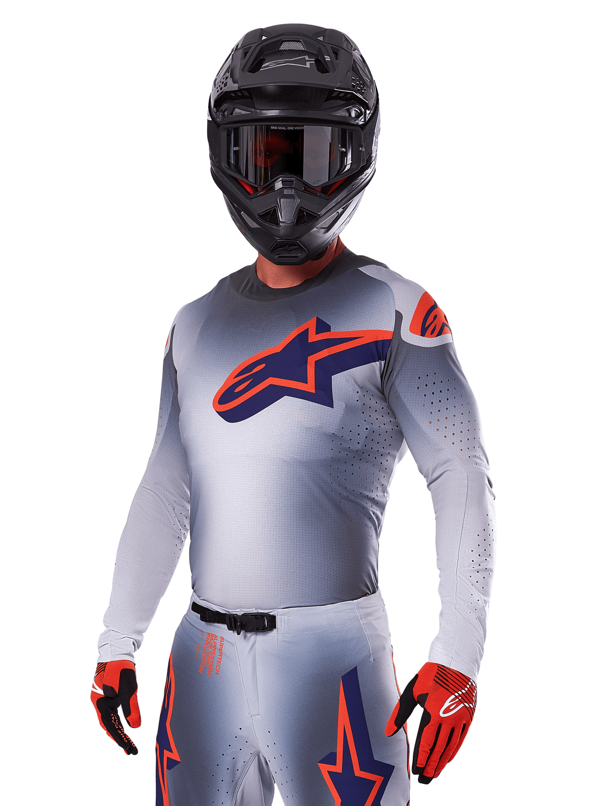 Piloto de motocross con el conjunto de equipo Alpinestars 2025 Supertech Lipan, jersey y pantalones grises con detalles en azul marino y naranja, casco negro mate con gafas, y guantes rojos y negros, equipamiento de alto rendimiento para carreras todoterreno
