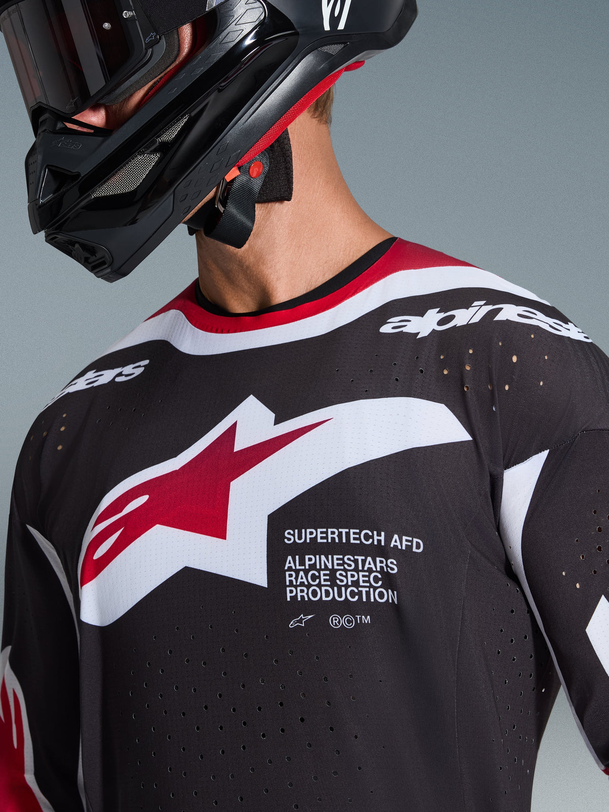 Alpinestars 2026 Supertech AFD Vista Jersey, close-up of a motocross rider wearing a black jersey with red and white accents, featuring a large white and red Alpinestars logo, laser-cut ventilation perforations, and professional racing fit, paired with a black helmet.