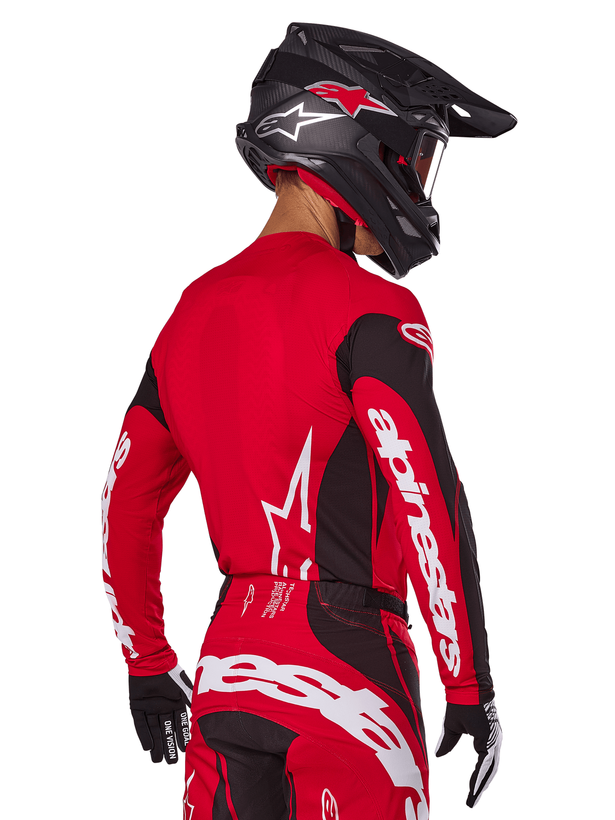 Piloto de motocross visto desde atrás con el conjunto Alpinestars 2025 Techstar Dreem, jersey rojo y negro con marca blanca en las mangas, pantalones rojos y negros a juego con un logotipo blanco llamativo en la parte trasera, casco de carbono negro con detalles rojos, guantes negros y blancos, equipamiento profesional para carreras todoterreno.