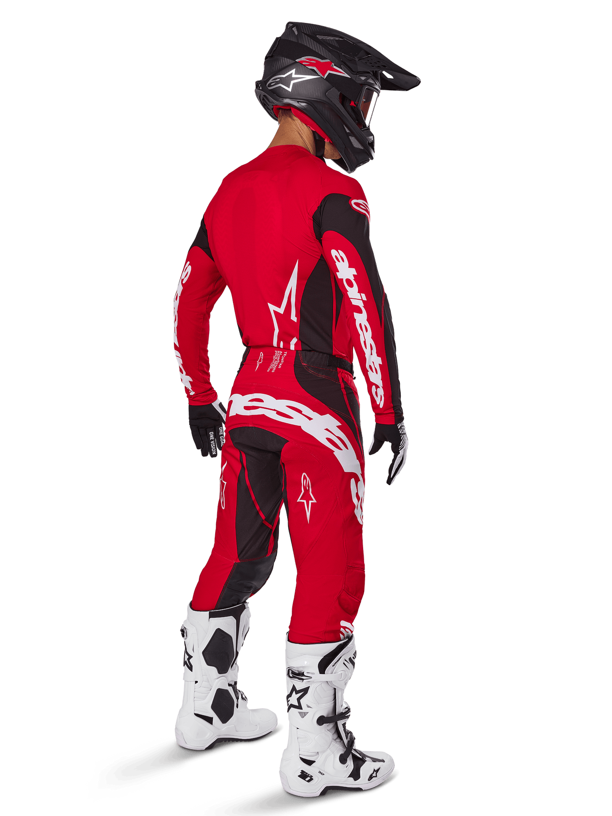 Piloto de motocross con el conjunto de equipo Alpinestars 2025 Techstar Dreem en rojo brillante y negro, con logotipos blancos en el jersey y los pantalones, acompañado de un casco negro, botas blancas y negras y guantes negros y blancos, vista trasera de tres cuartos.