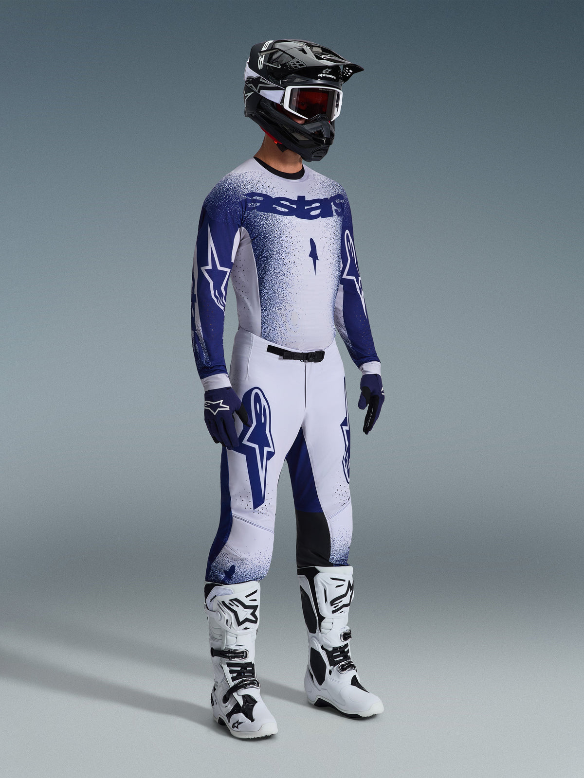 Alpinestars 2026 Supertech Scenz Gear Set, Motocross rider wearing white and navy blue racing jersey and pants with a gradient stipple effect, features bold Astars branding, paired with a black and white helmet, navy gloves, and white motocross boots.
