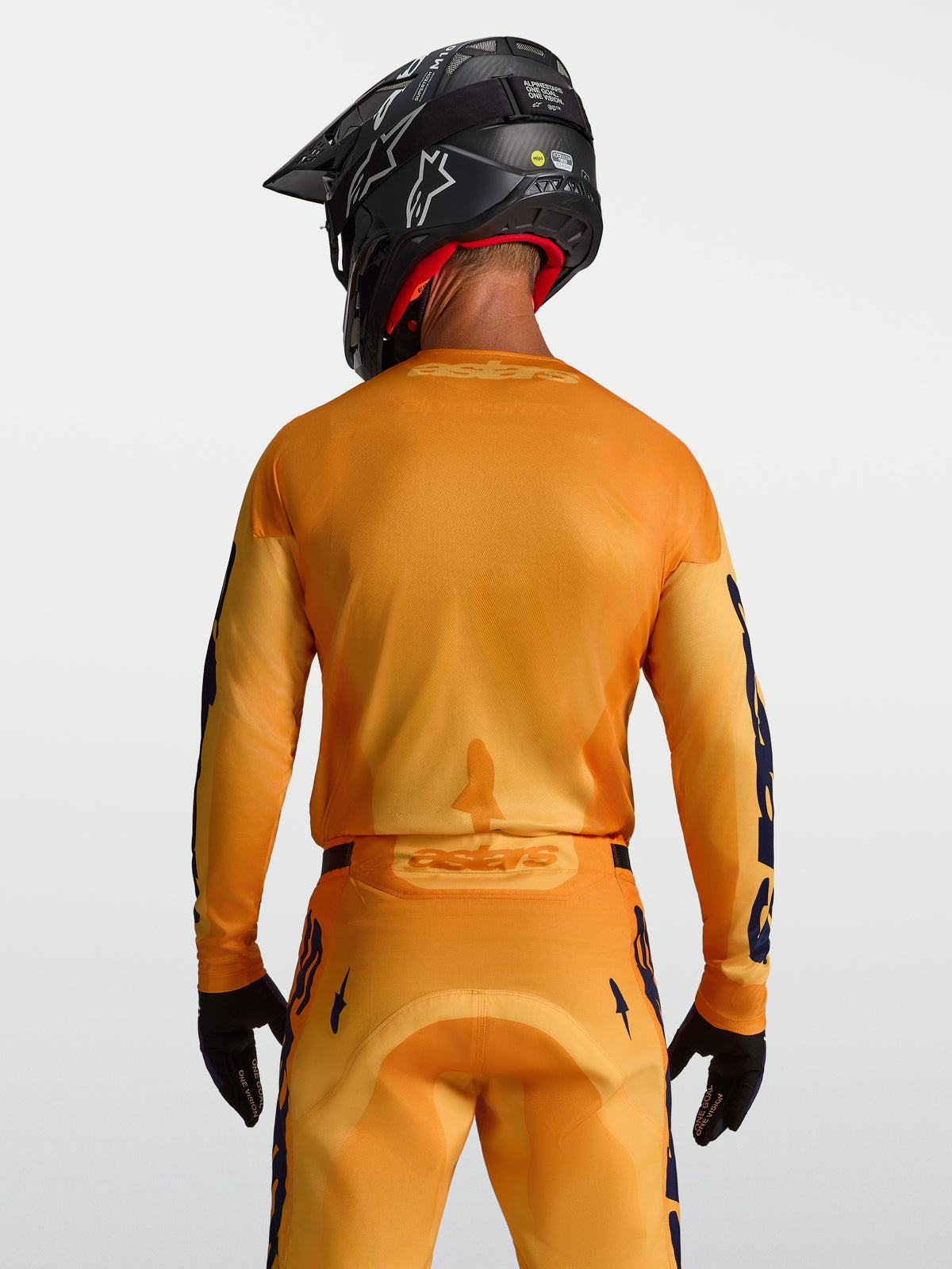 Alpinestars Racer Amber, jersey de motocross para hombre, naranja y dorado, paneles de malla transpirable, vista trasera en modelo con casco